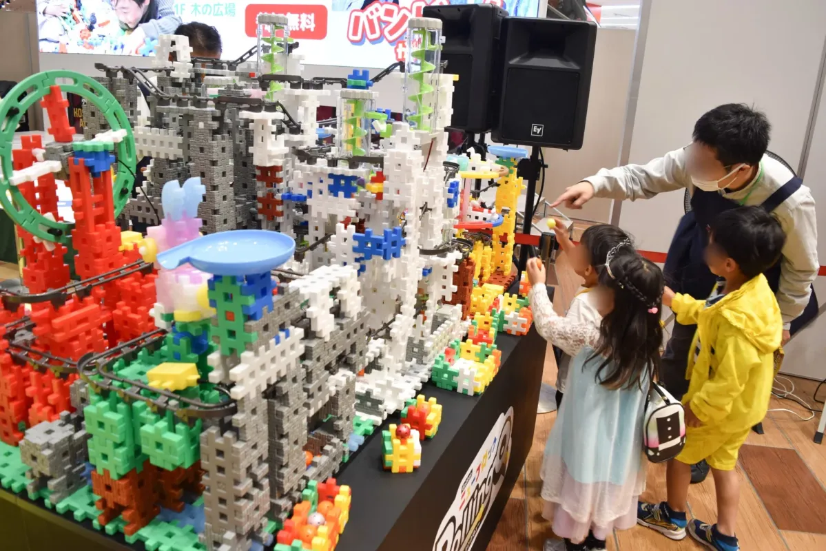 子供たちがブロックのおもちゃで遊んでいる様子。大人が子供たちに遊具の使い方を教えている。