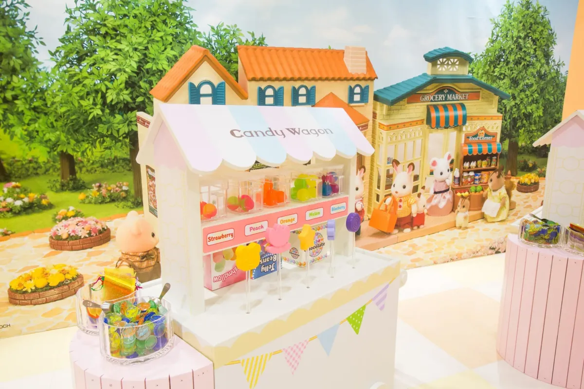 おもちゃのキャンディワゴンとお店が並んだ、可愛らしいジオラマの写真。キャンディワゴンには、様々なフレーバーのキャンディが並び、お店の前にはシルバニアファミリーの人形たちがいる。