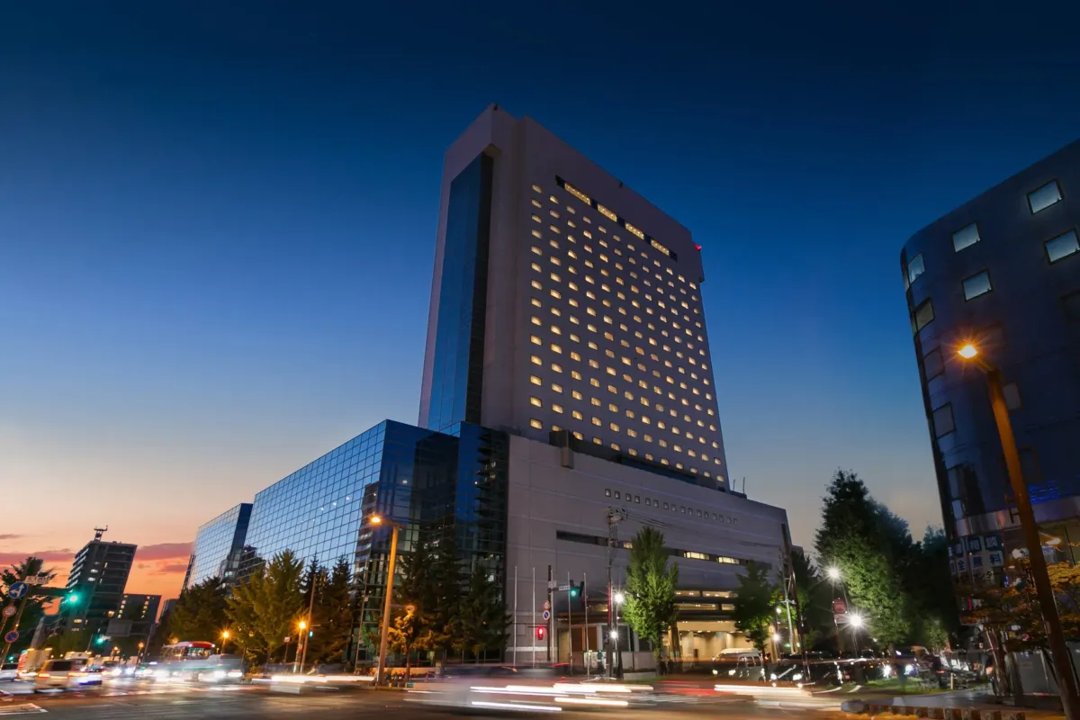 夜の街並み。高層ビルがそびえ立ち、街灯が周囲を照らしている。空は夕焼けと夜空が混ざり合い、美しいコントラストを生み出している。
